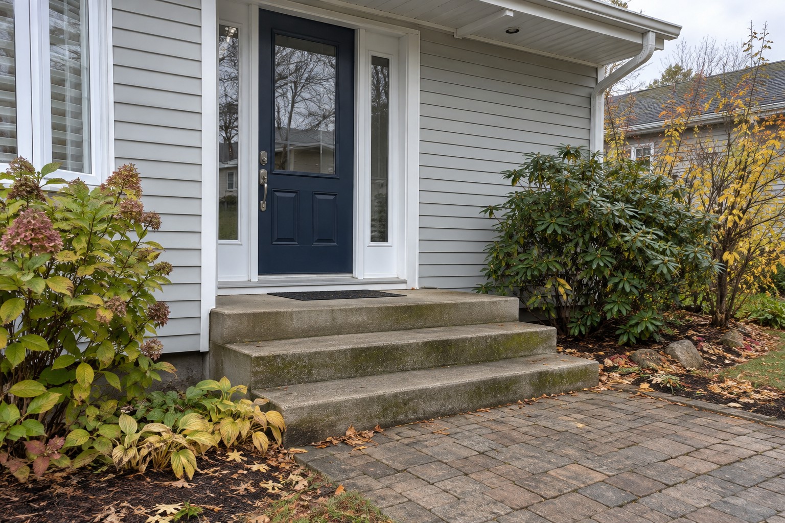 Illustrative entrance with a navy door, white frames, concrete steps with green buildup and an interlock walkway