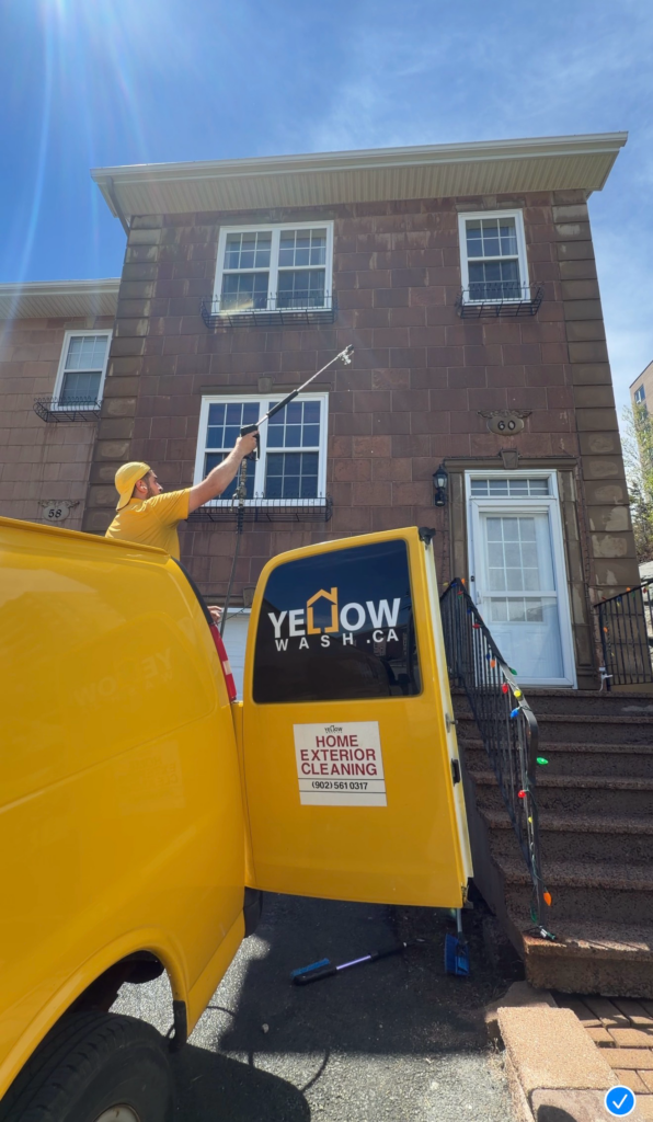 Yellow Wash team member cleaning a house beside the yellow company van