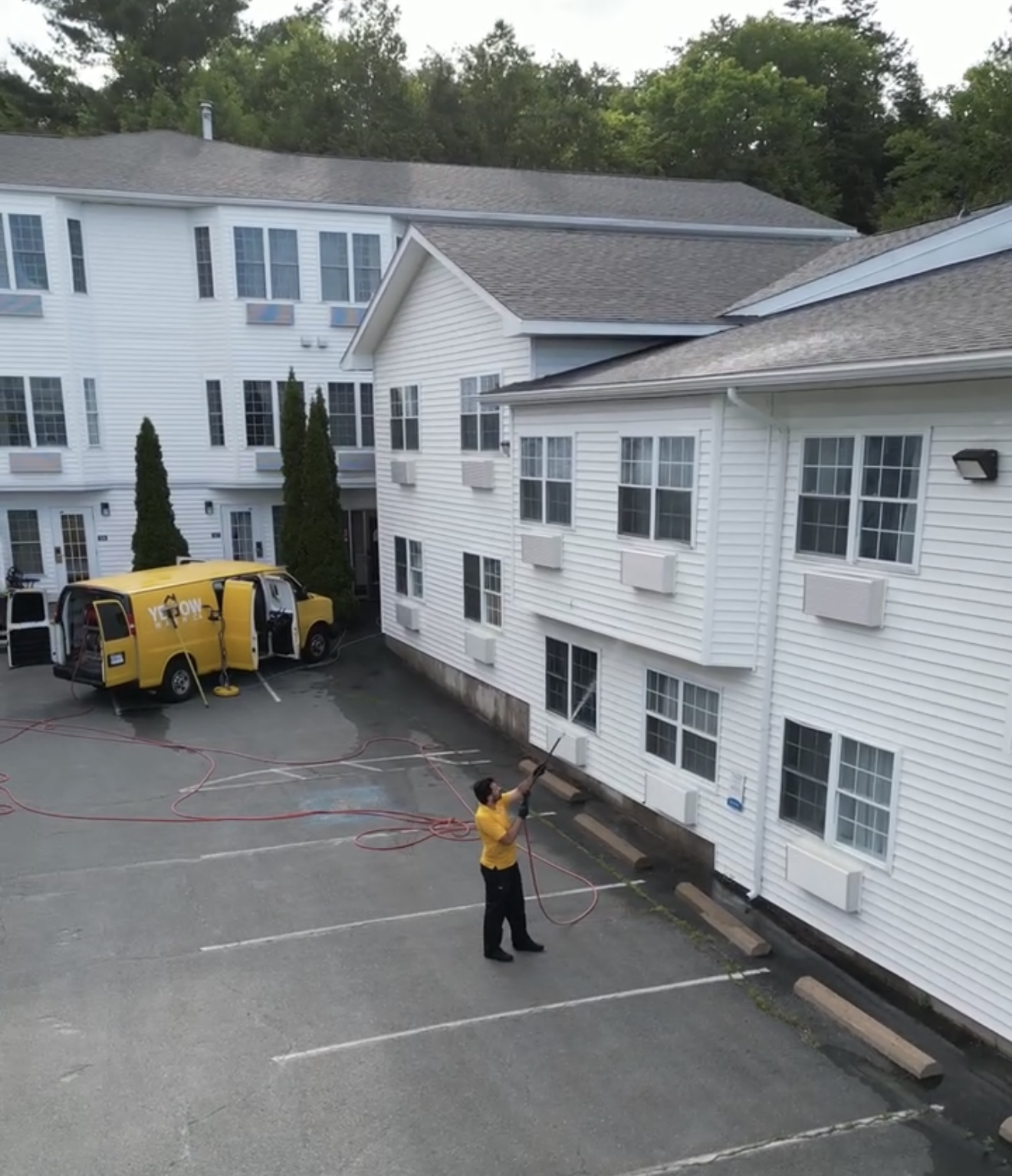Yellow Wash technician washing a hotel exterior beside the yellow service van